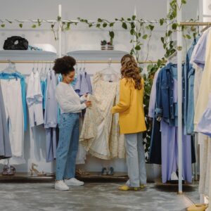 Two women shopping for trendy outfits in a modern clothing boutique filled with colorful garments.